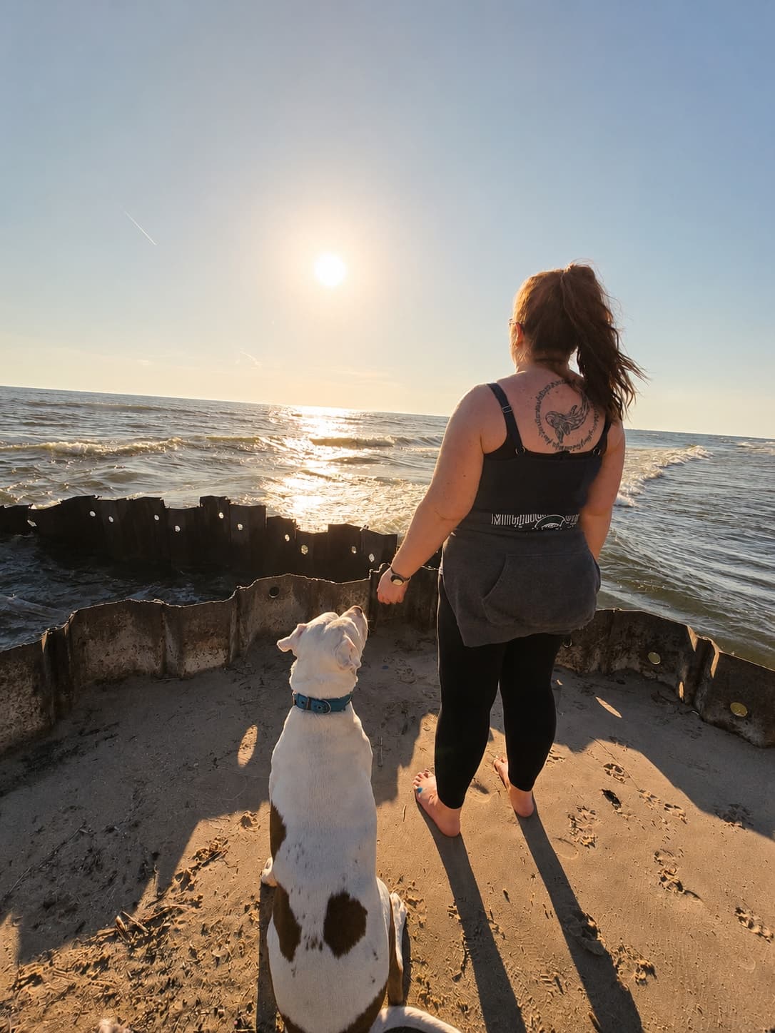 Racheal from behind on a Lake Michigan beach at golden hour, her dog Ziga sitting beside her.