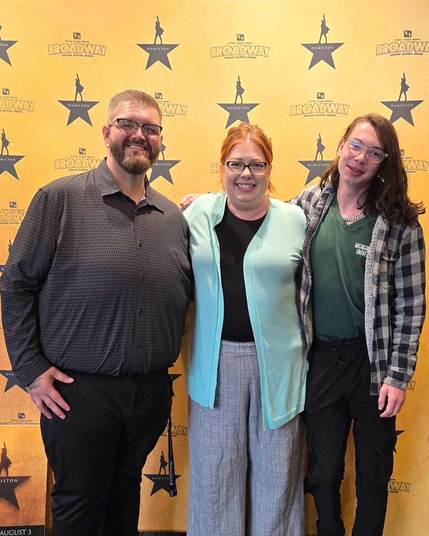 Racheal with family in front of a yellow Hamilton backdrop at the theater.