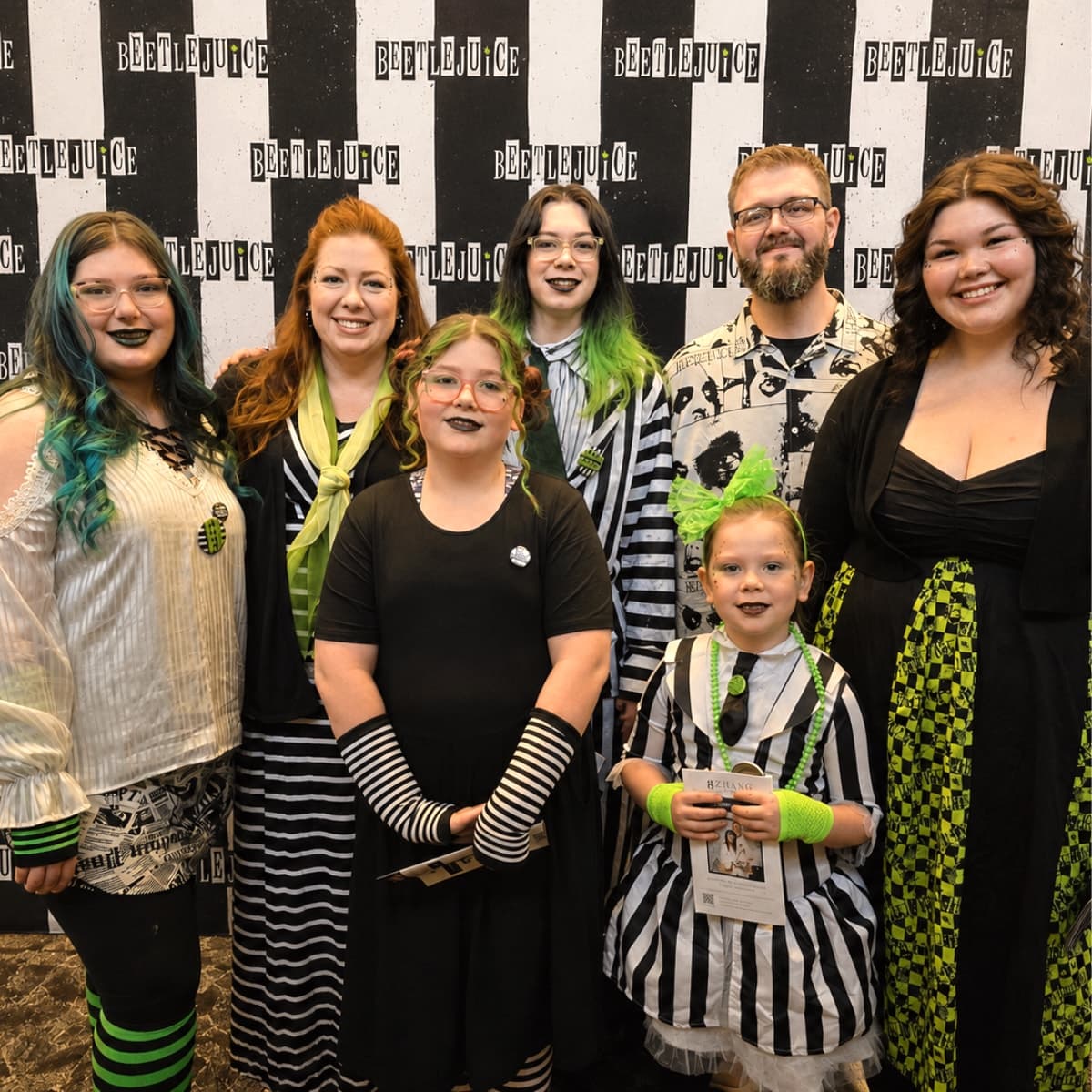 Racheal and her family in Beetlejuice costumes in front of the striped backdrop.