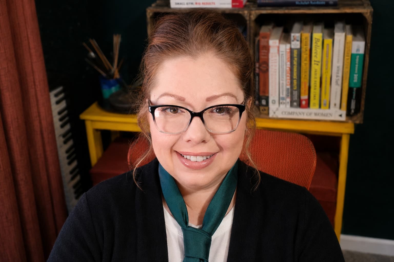 Racheal Blackmore at her desk in front of a crate of books, wearing glasses and a green tie.